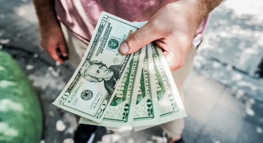 Dłoń trzyma kilka banknotów po 20 dolarów, symbolizując sposób, jak zarabiać więcej.