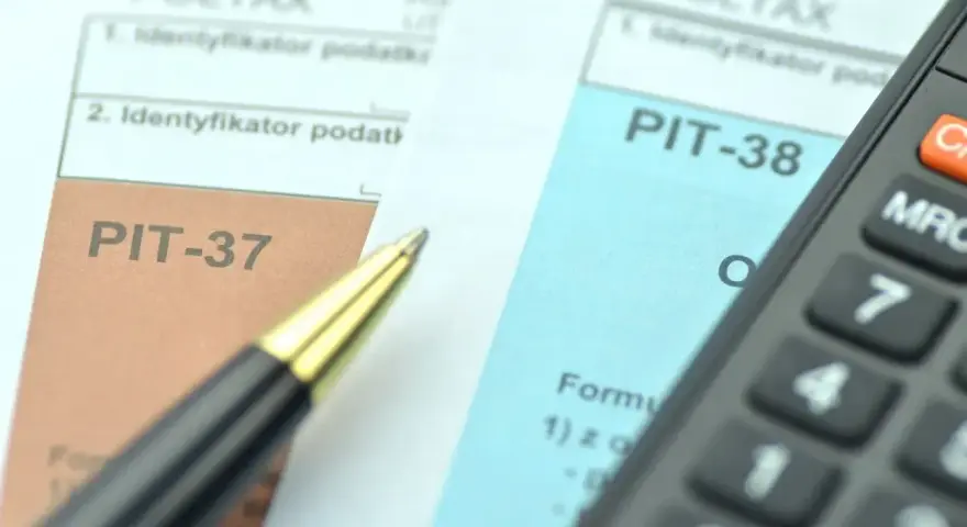 Dwa formularze podatkowe, PIT-38 i PIT-37, leżą obok siebie, gotowe do wypełnienia. Obok leży długopis i kalkulator.