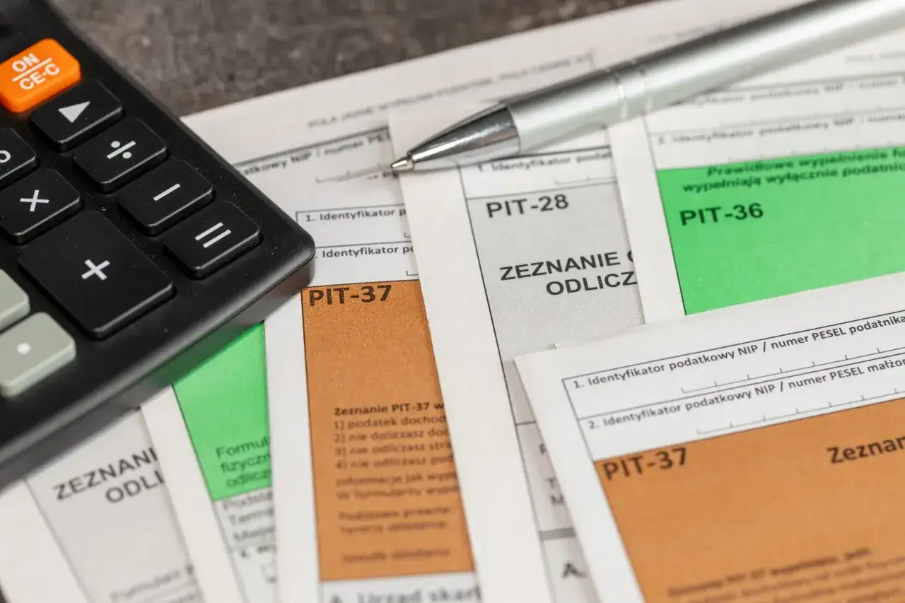Kalkulator i długopis leżą na dokumentach PIT. Zastanawiasz się, jak obliczyć ile dostanę zwrotu podatku? Te formularze pomogą Ci to ustalić.