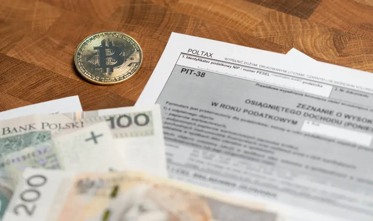 Złoty bitcoin i polskie banknoty leżą obok formularza PIT-38, sugerując potencjalną dużą niedopłatę podatku od kryptowalut.