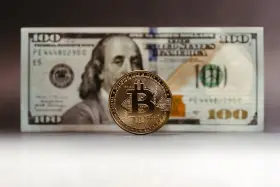 Złoty Bitcoin na tle banknotu 100 dolarów. Zastanawiasz się, jak rozliczyć podatek od zysku z kryptowalut?