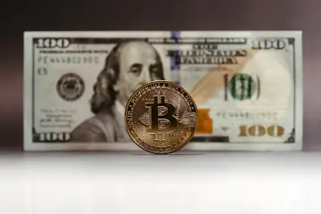 Złoty Bitcoin na tle banknotu 100 dolarów. Zastanawiasz się, jak rozliczyć podatek od zysku z kryptowalut?