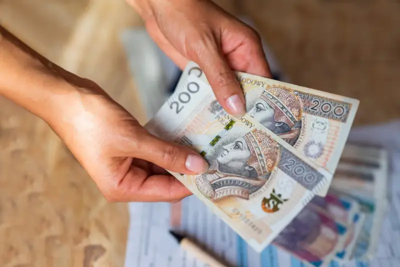 Dłonie trzymają banknoty 200 zł. Czy na lokatę można wpłacać pieniądze co miesiąc?